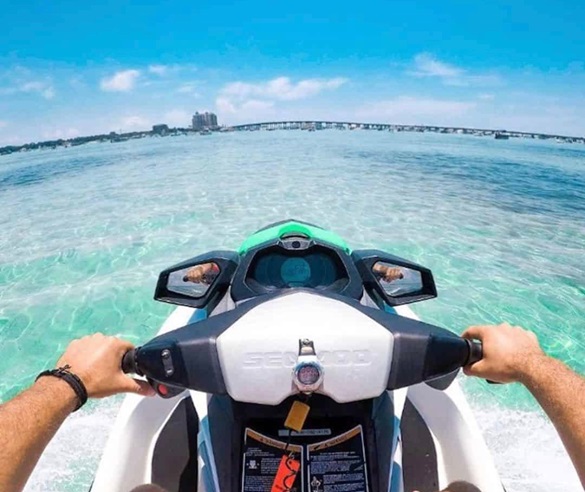 View of the front of a jet ski riding across waves, with a person's hands gripping the handles