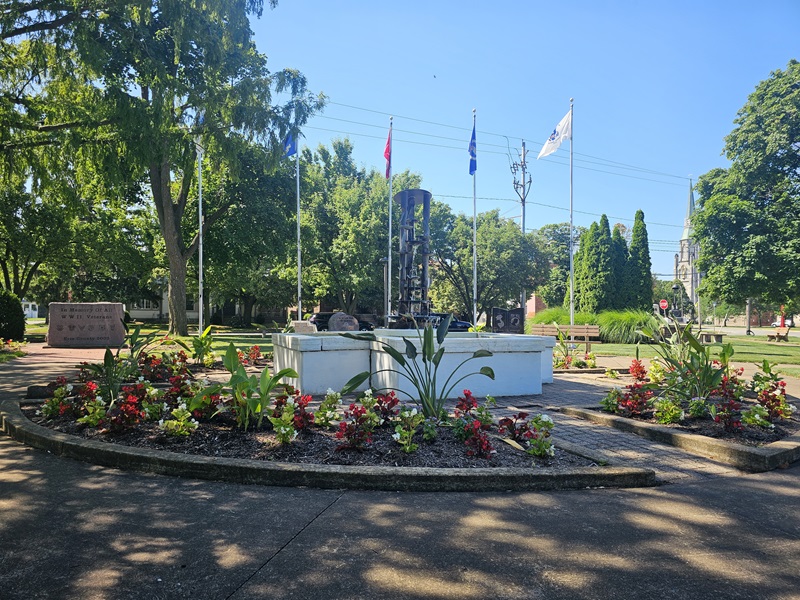 View of the centerpiece fountain sculpture, with flowerbeds in front of it and trees in the background