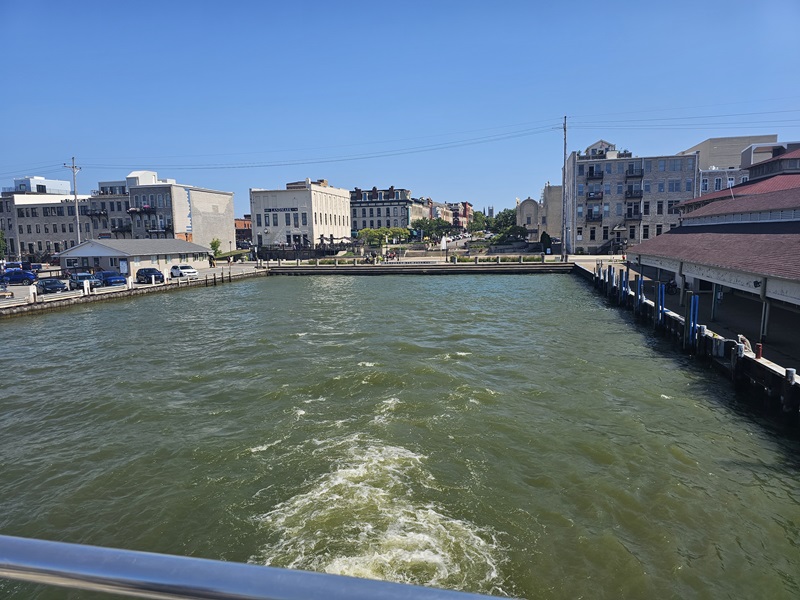 View of the bay behind the ferry railing and the surrouding downtown area as the ferry is taking off