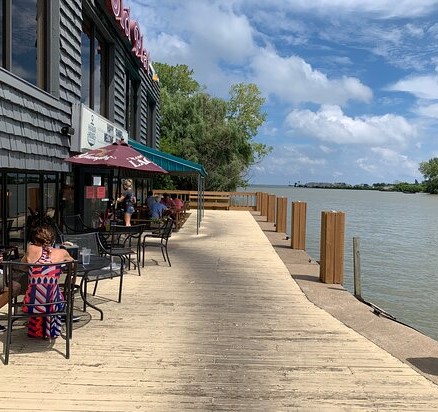 View of Harbor House's umbrellaed patio tables along the dock on the left and the Huron River on the right